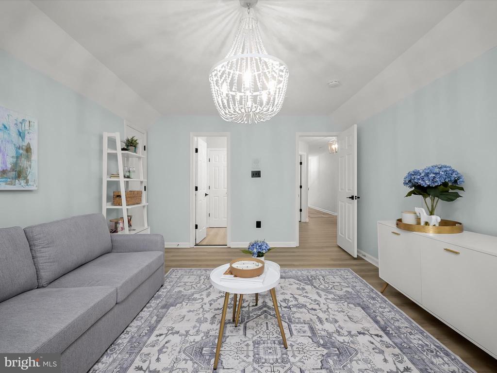 Staged living room with a gray sofa, patterned rug, and beaded chandelier.