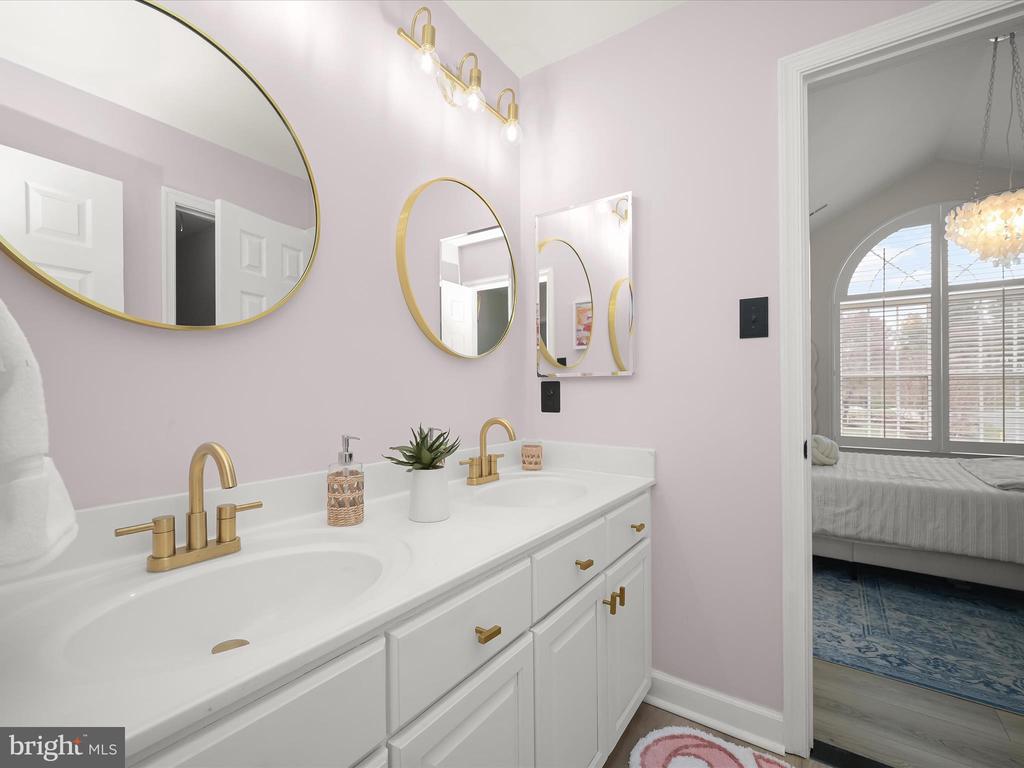 Bathroom with a white double vanity, gold fixtures, pale pink walls, and gold-framed mirrors.