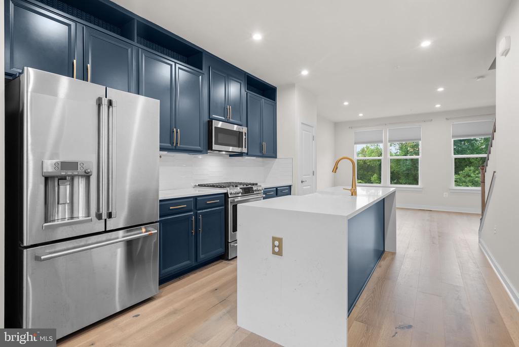 Kitchen with navy cabinets, stainless steel appliances, and a white island with a brass faucet.