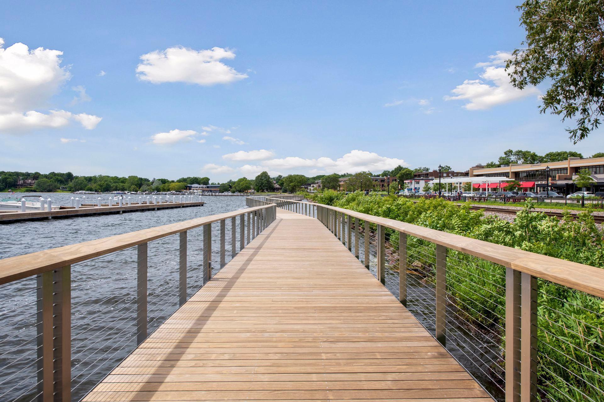 A wooden boardwalk curves beside a lake, with boat docks and lakeside shops.
