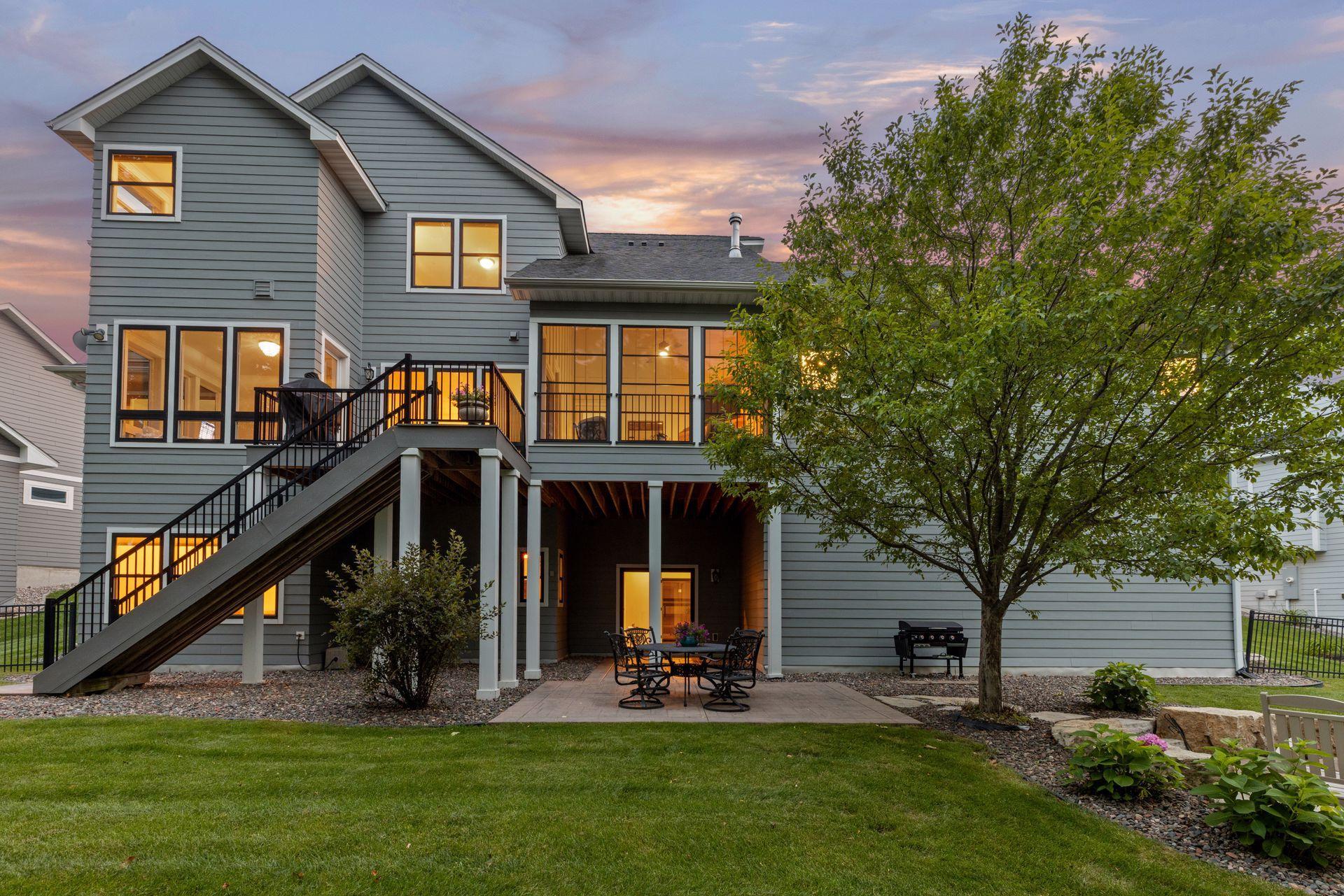 Gray two-story home with a raised deck, long staircase, and patio at dusk.