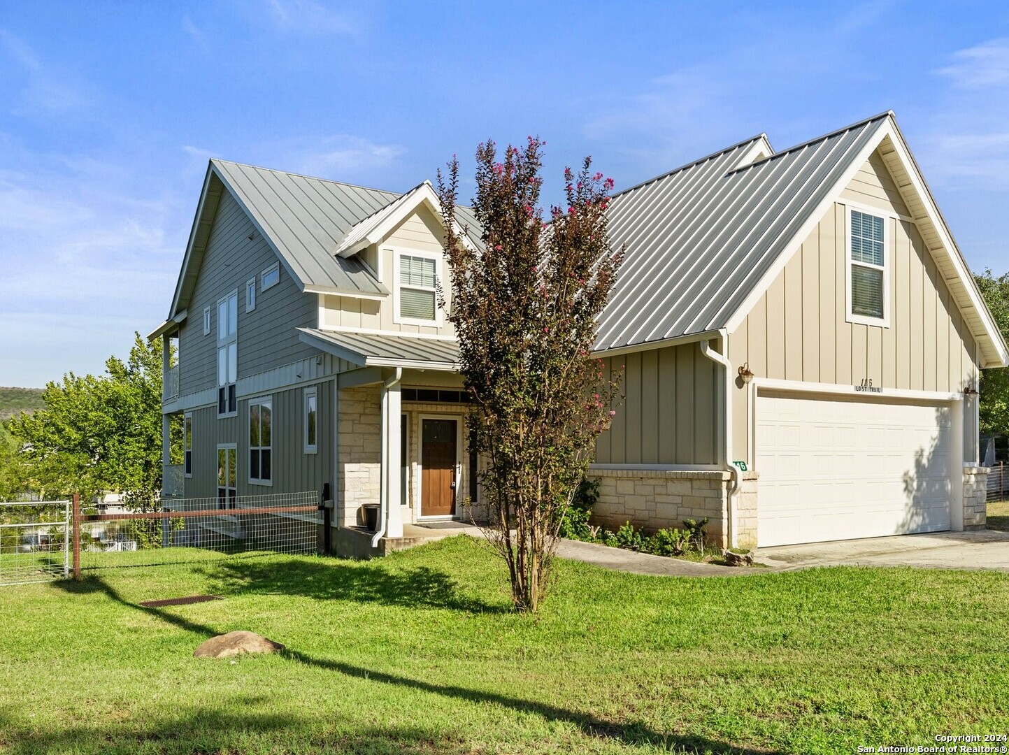 Two-story gray-green and cream home with a metal roof, stone accents, and a white garage door.