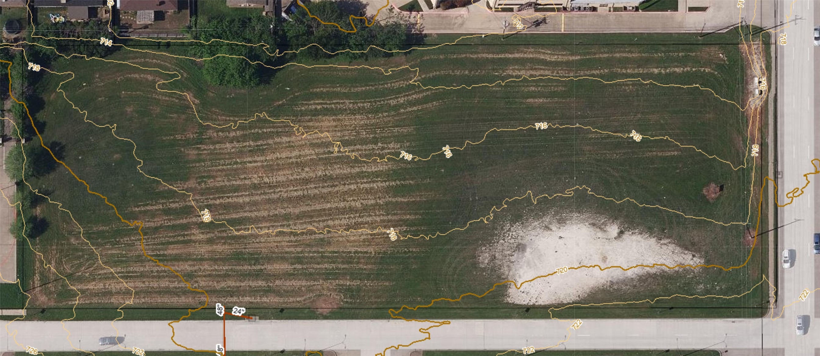 Aerial view of a vacant grassy parcel with topographic contours and a pale cleared area.