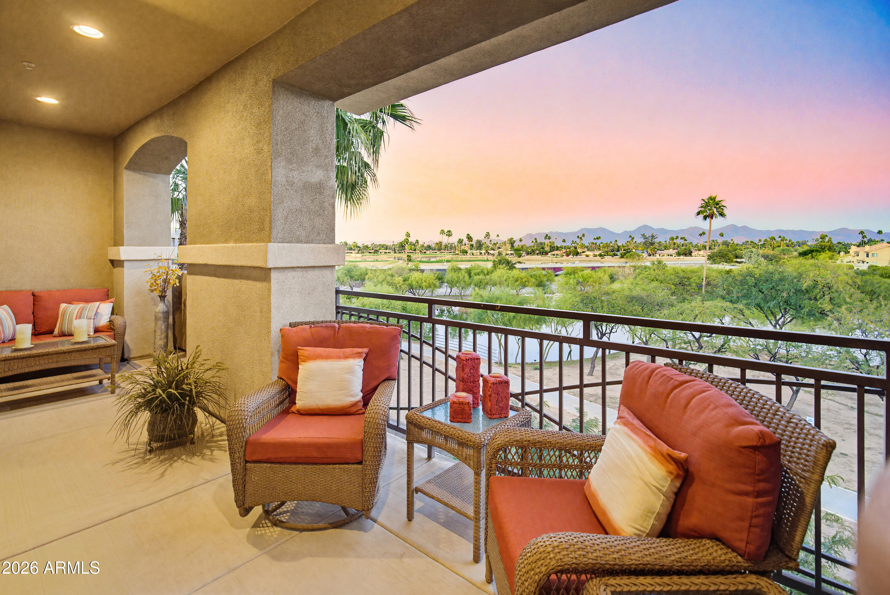 Covered balcony with wicker seating overlooking a waterway and distant mountains at sunset.