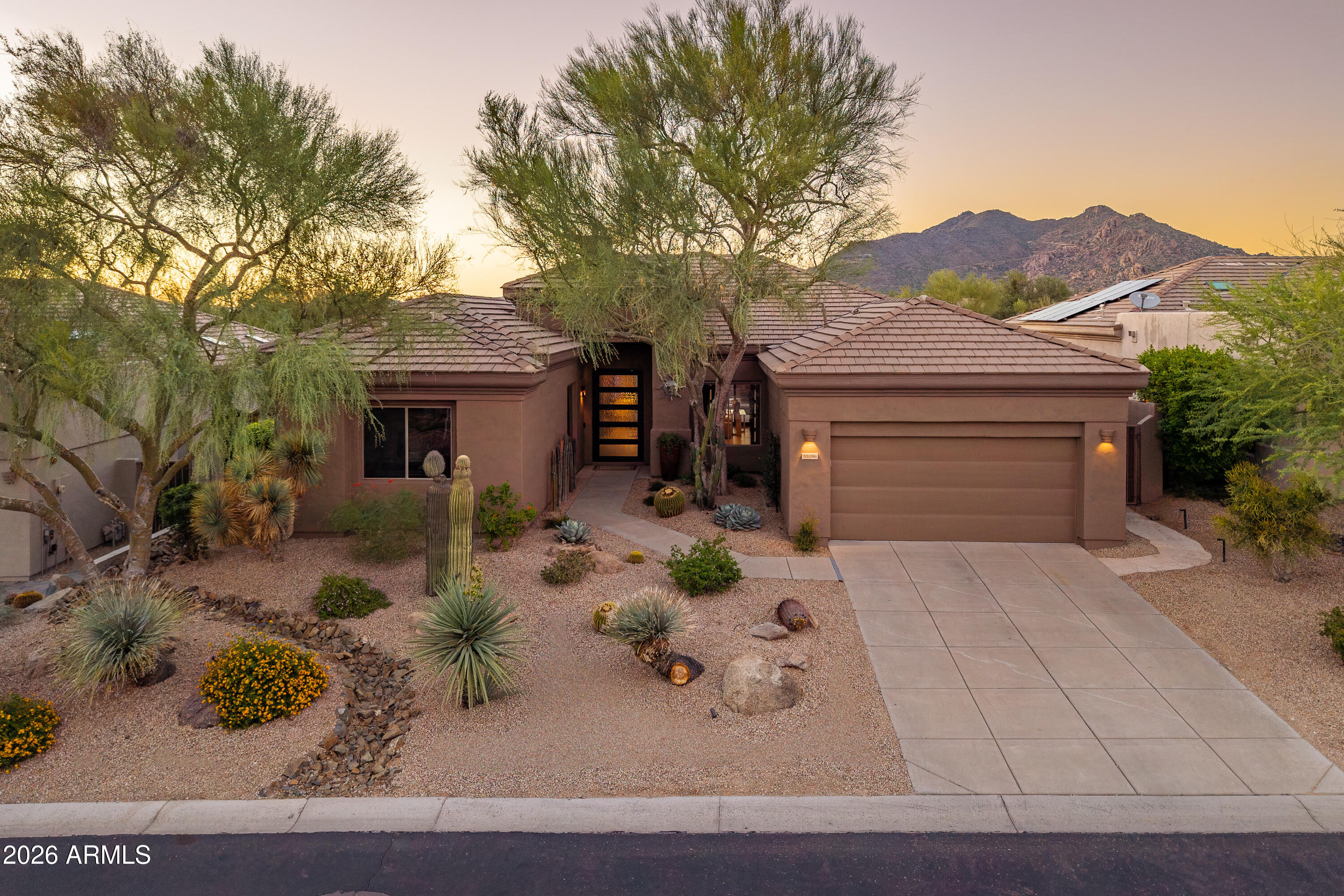 Southwestern home with desert landscaping, a two-car garage, and mountains behind it at sunset.