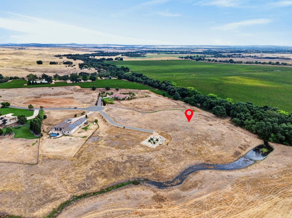 Aerial view of a dry parcel marked by a red pin beside a creek and cultivated fields.