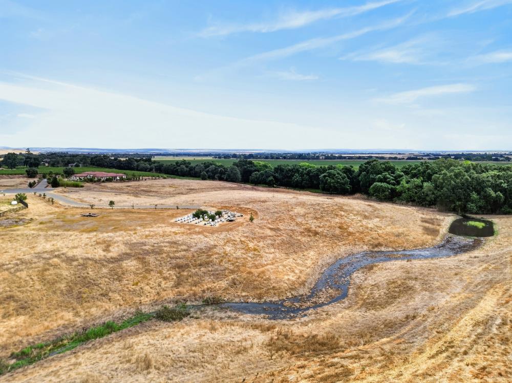 Aerial view of dry open land with a winding creek and distant tree line.
