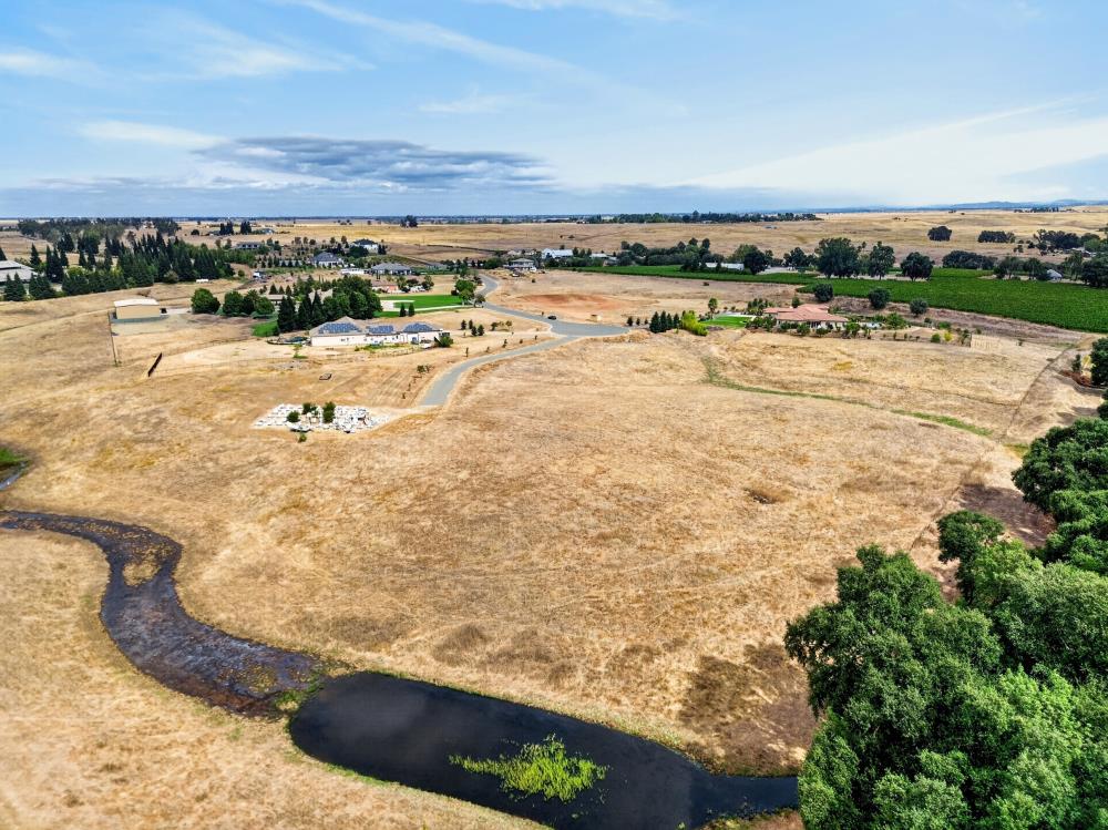 Aerial view of dry open land with a winding creek and pond in the foreground.