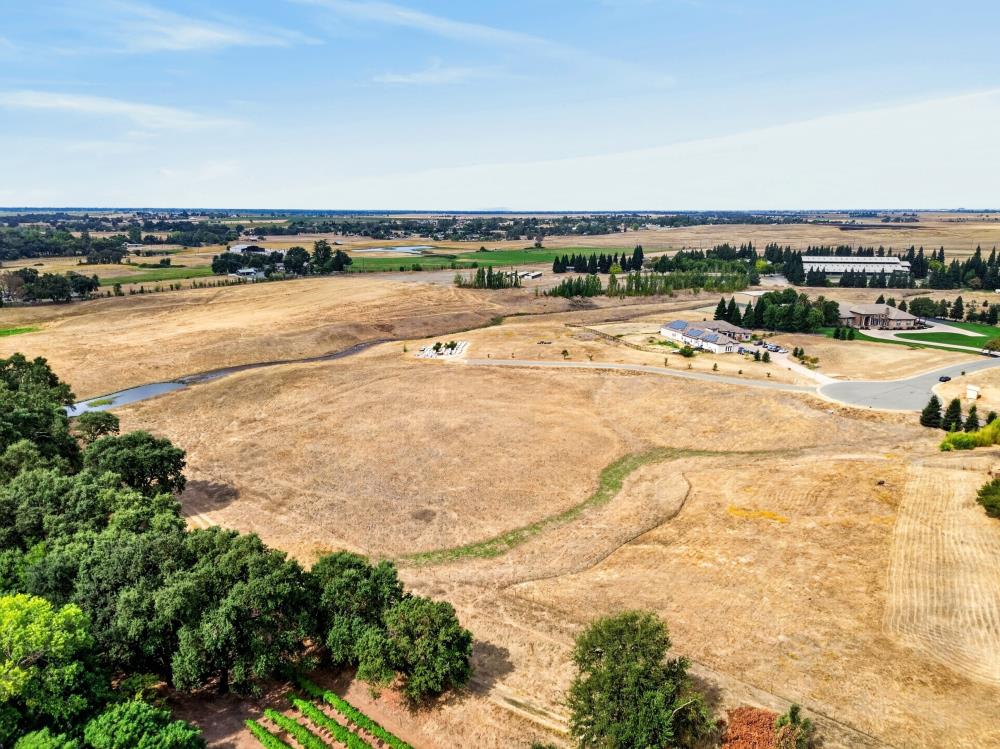 Aerial view of dry open land beside a curving road, with trees and nearby homes.
