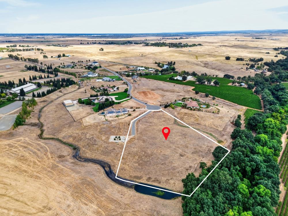 Vacant parcel outlined beside a tree-lined creek, with a road and rural fields nearby.