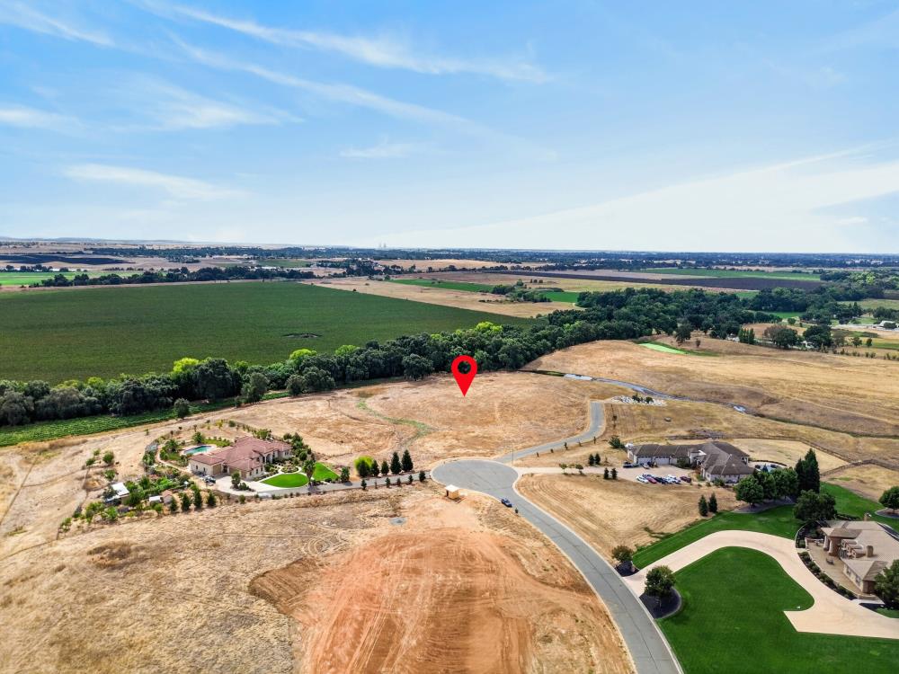 Aerial view of a vacant lot marked by a red pin, beside a curving road and neighboring homes.