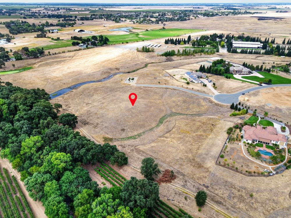 Vacant dry lot marked by a red pin, bordered by trees, fields, and a curving road.