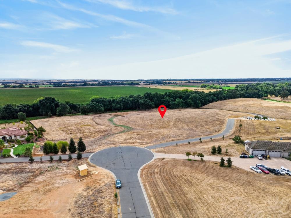 Vacant lot marked by a red pin beside a cul-de-sac, with fields and a wooded strip beyond.