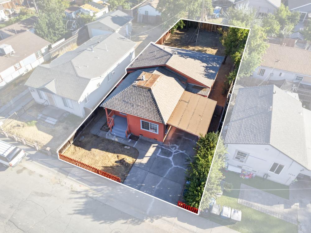 Aerial view of a red house with a fenced yard and driveway, outlined among neighboring homes.