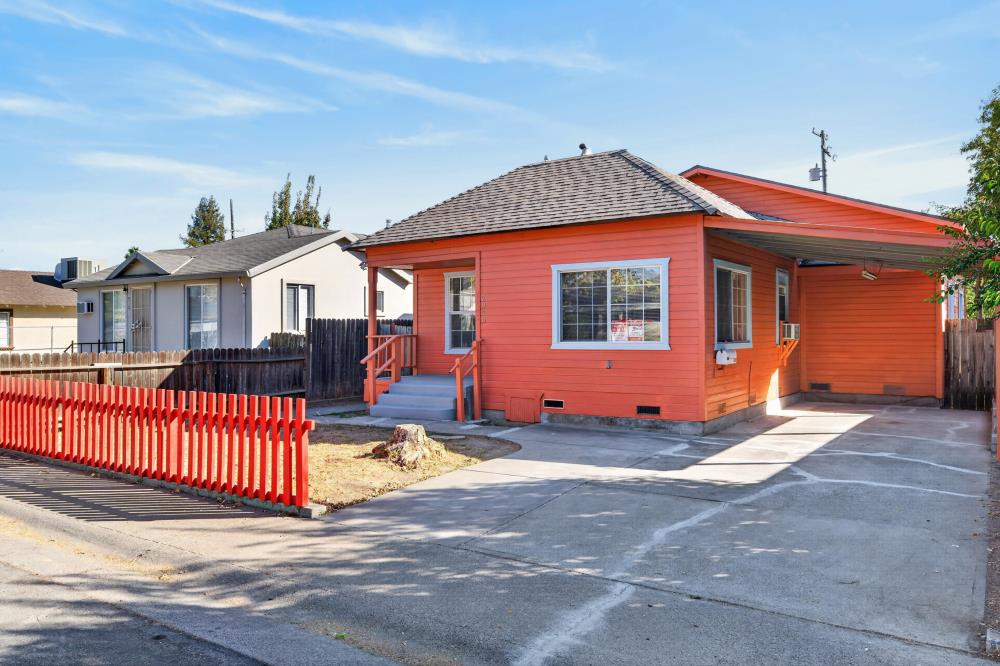 Orange single-story house with a covered carport, wide driveway, and red picket fence.