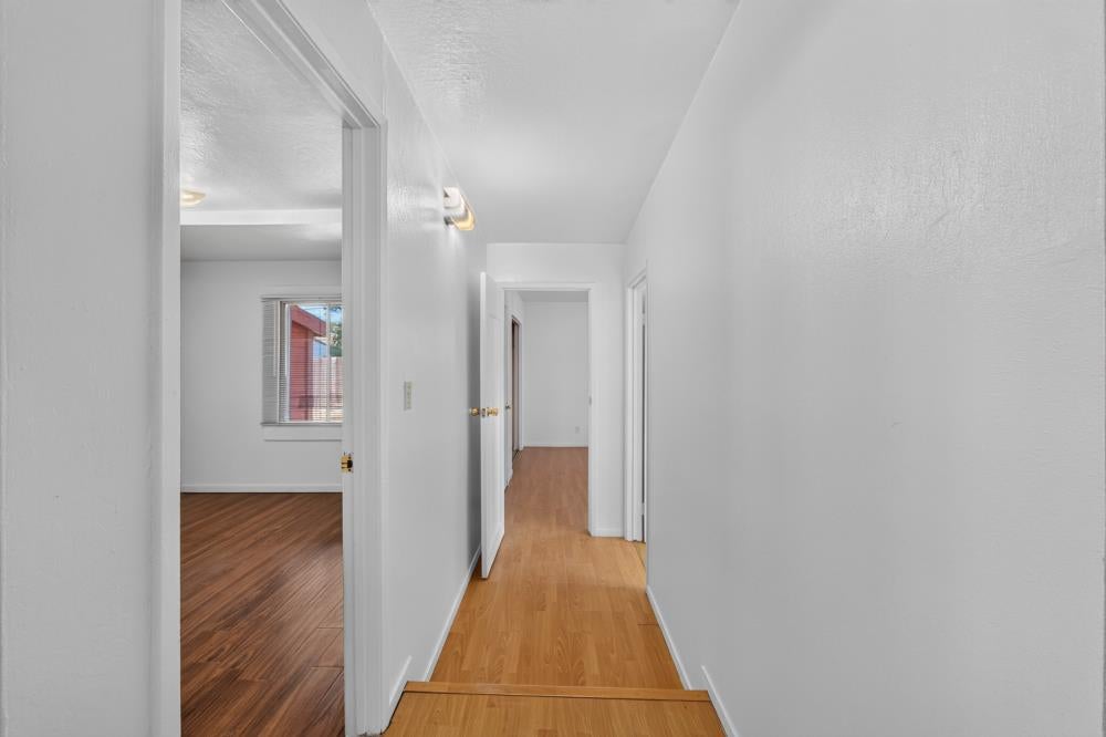 Empty hallway with light wood flooring and doorways to adjoining rooms.