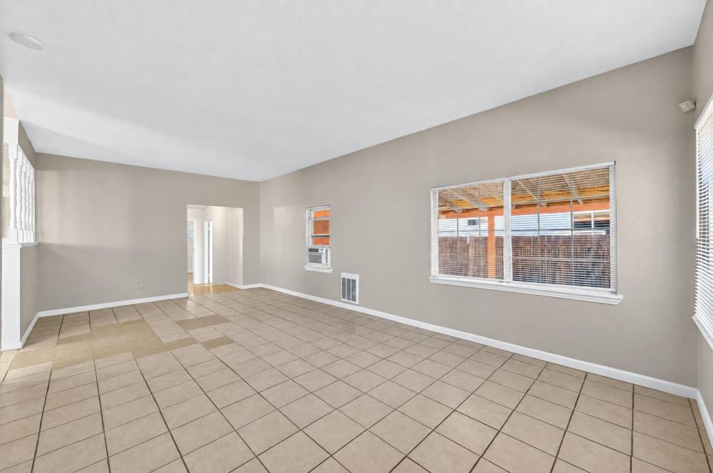 Empty living room with beige tile floors, neutral walls, and wide windows with blinds.