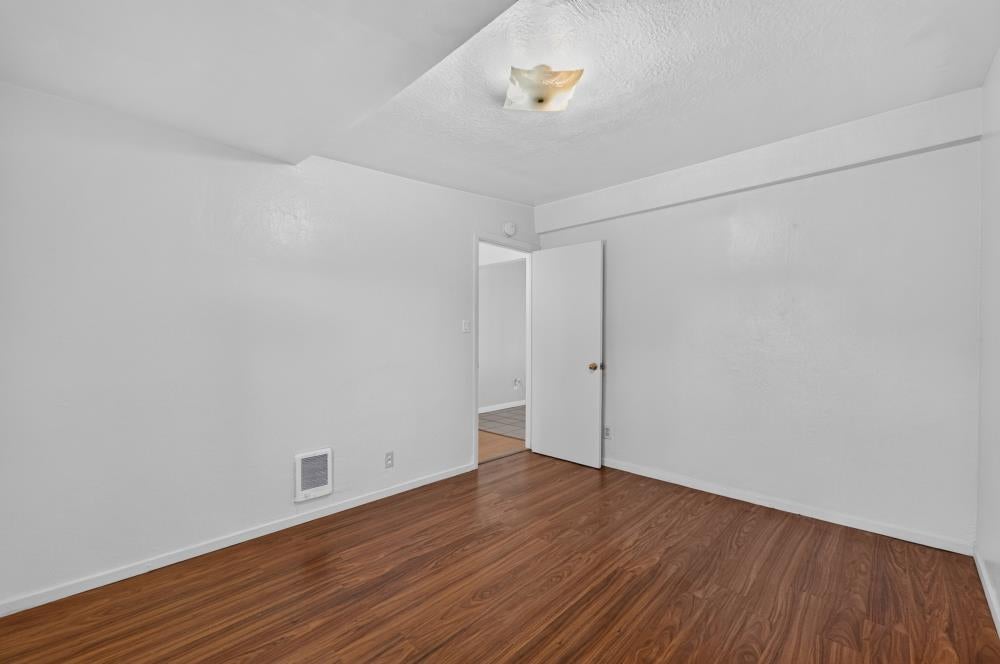 Empty room with reddish-brown wood-look flooring, white walls, and an open door.