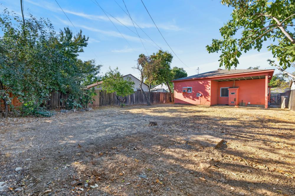 Fenced backyard with a red detached building, mature trees, and a broad dry yard.