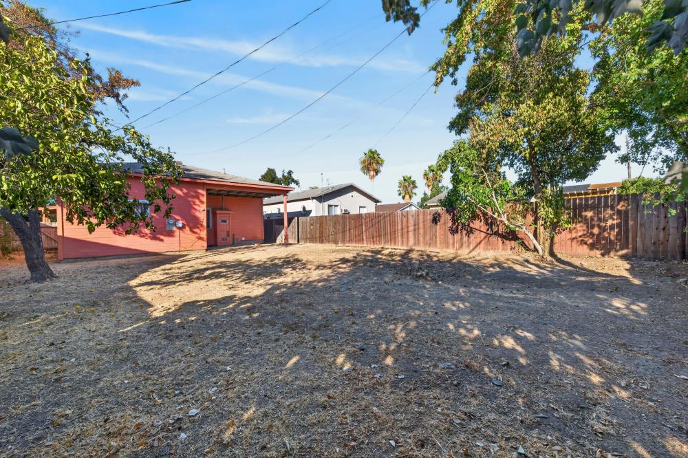 Dry backyard with mature trees, wooden fencing, and a red outbuilding.