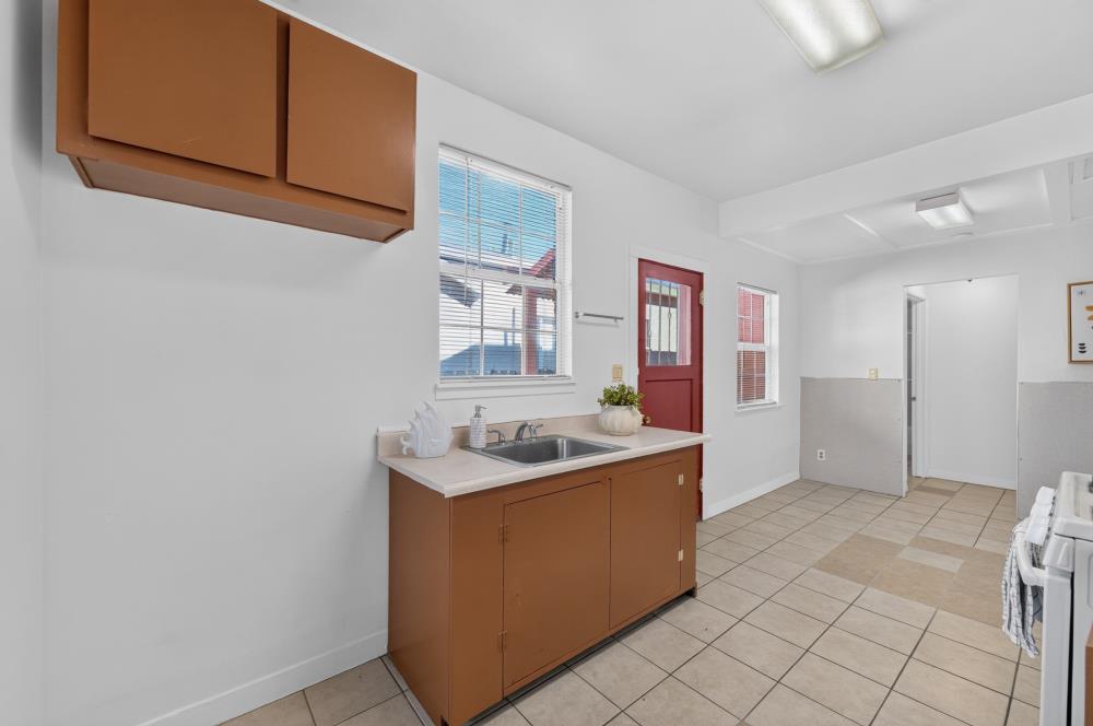 Kitchen with brown cabinets, a sink beneath the window, red door, and tiled floor.