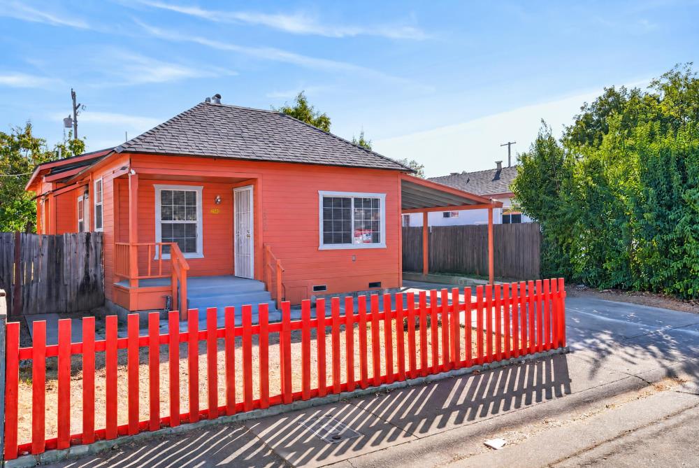 Red house with a covered porch, carport, and bright red picket fence.