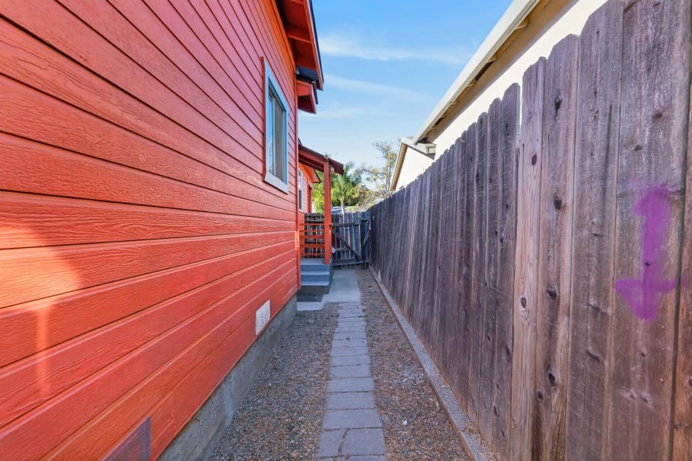 Side yard with a paver walkway between red house siding and a tall wooden fence.