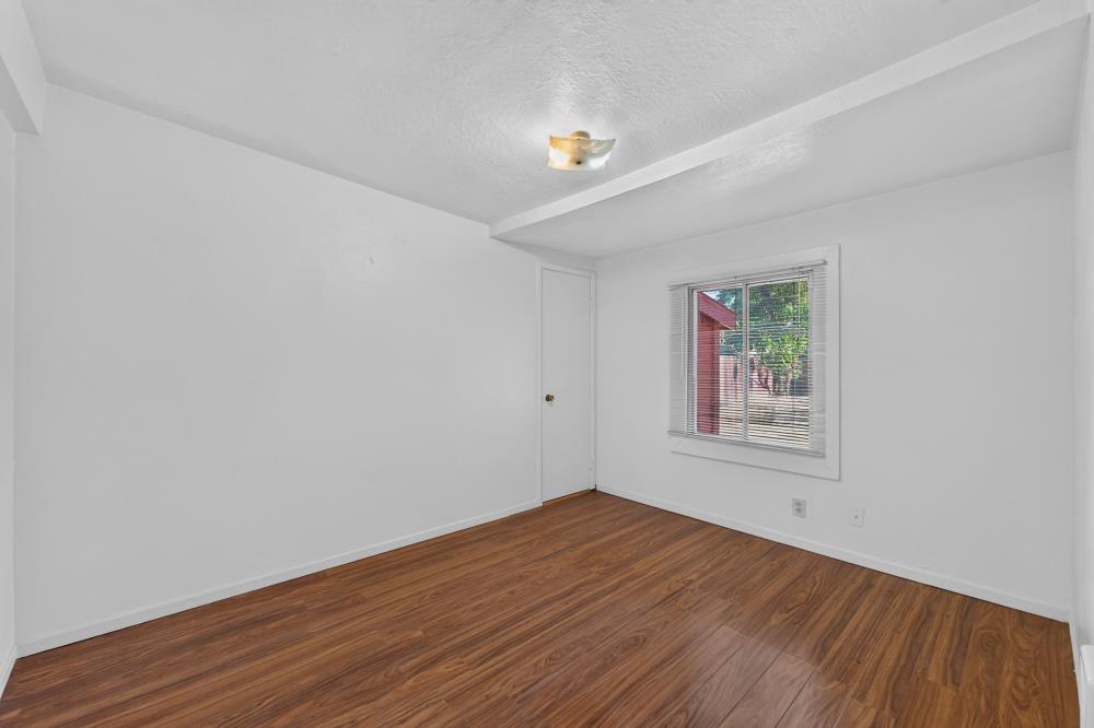 Empty bedroom with wood-look flooring, a closed door, and a window with blinds.