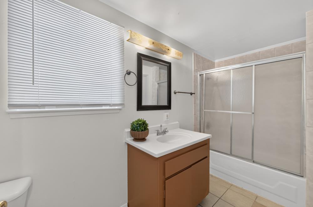 Bathroom with a brown vanity, white sink, and tub behind sliding frosted-glass doors.