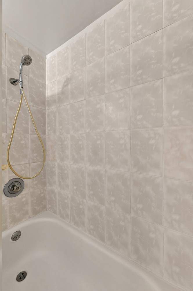 Bathtub and shower with pale tiled walls and a handheld showerhead.