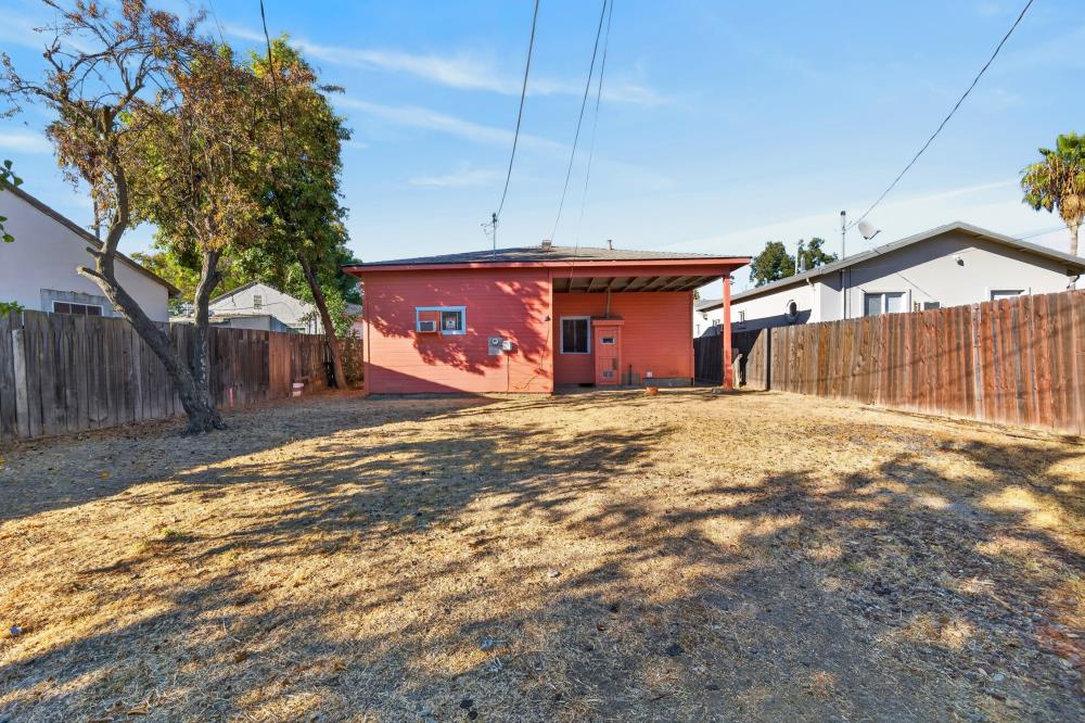 Red house with a covered patio behind a dry, fenced backyard.