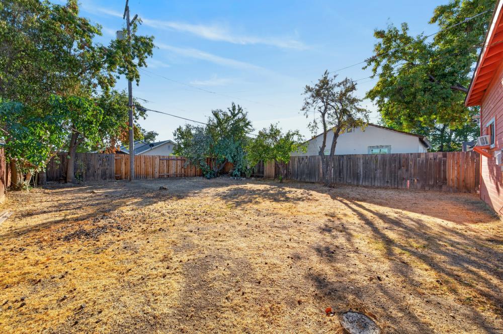 Mostly bare backyard enclosed by a wooden fence, with mature trees and the house’s red exterior wall.
