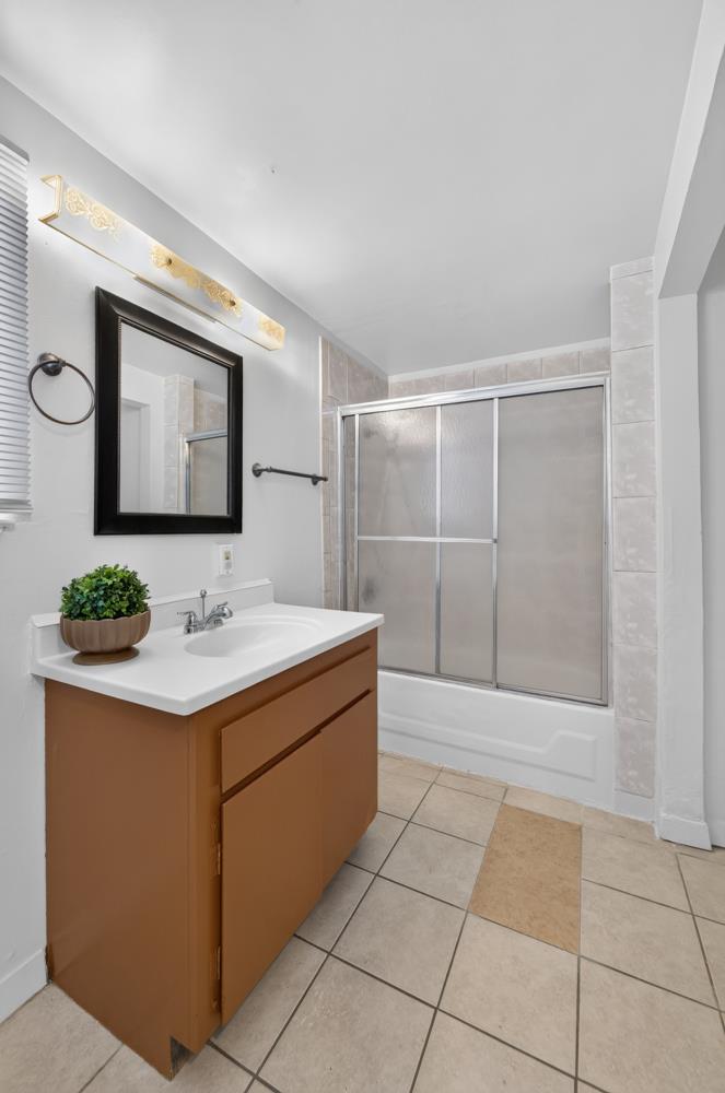 Bathroom with a brown vanity, black-framed mirror, and bathtub behind sliding glass doors.