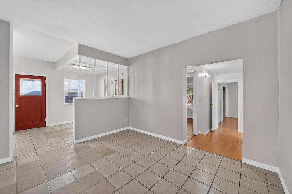 Tiled entry with a red front door, glass-panel partition, and doorway to a wood-floored hall.