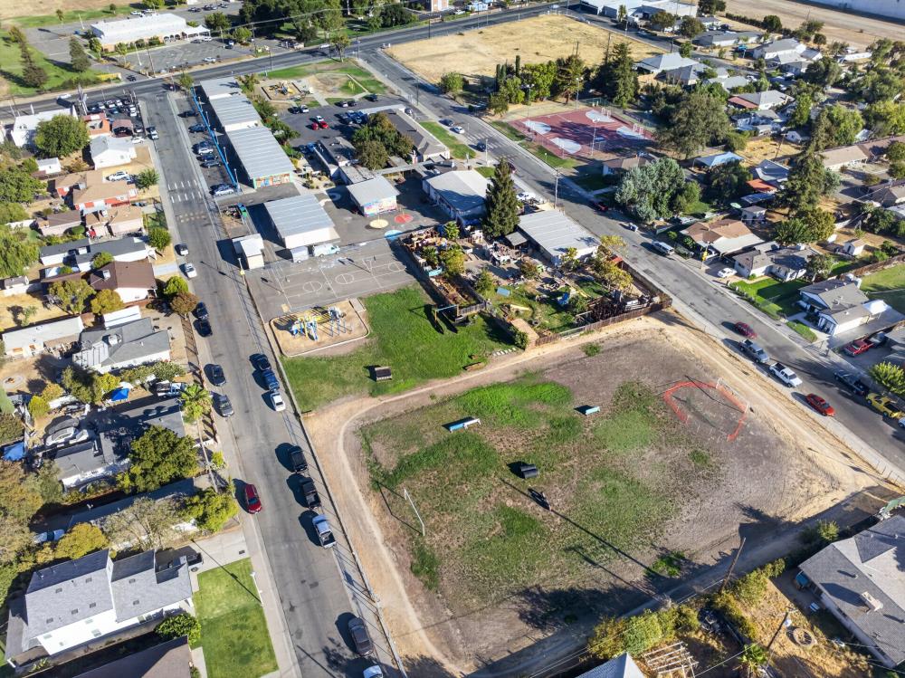 Aerial view of a vacant lot beside homes, streets, and recreation courts.