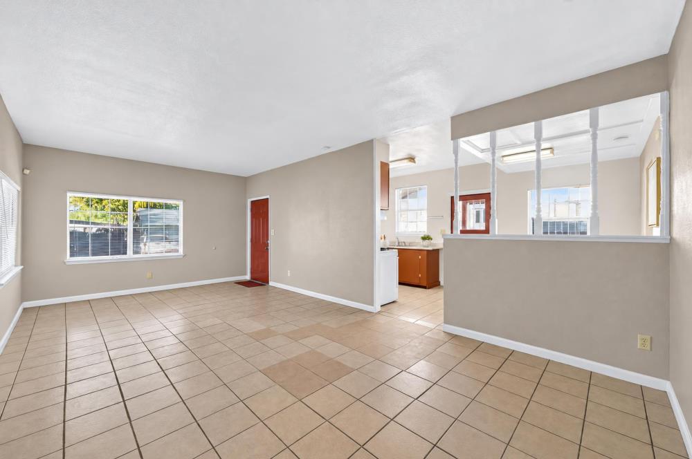 Empty tiled living area with a wide pass-through opening into the kitchen.