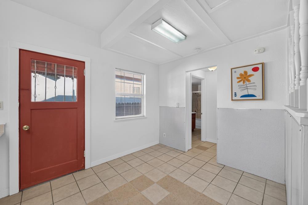 Tiled entryway with a red front door, window with blinds, and framed flower artwork.