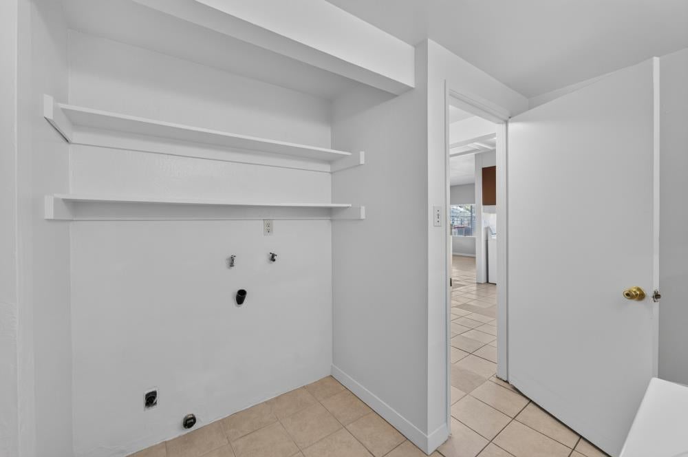Empty laundry room with wall shelves, washer hookups, and a tiled floor.