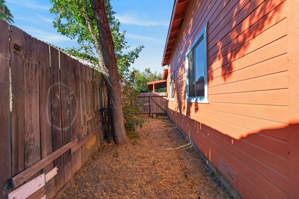 Side yard with orange-red siding, a blue-trimmed window, wooden fence, and mature tree.