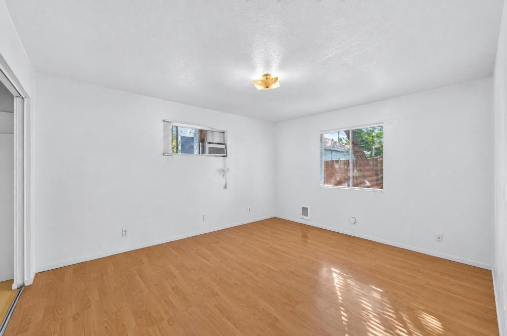 Vacant room with light wood floors, two windows with blinds, and a ceiling light.