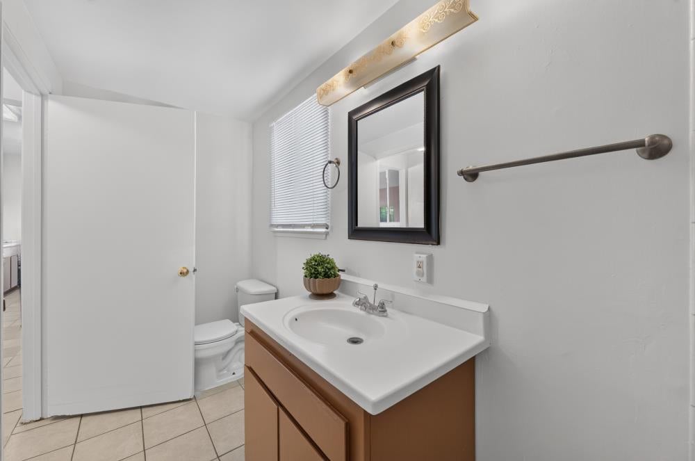 Bathroom with a brown vanity, white sink, framed mirror, and tiled floor.