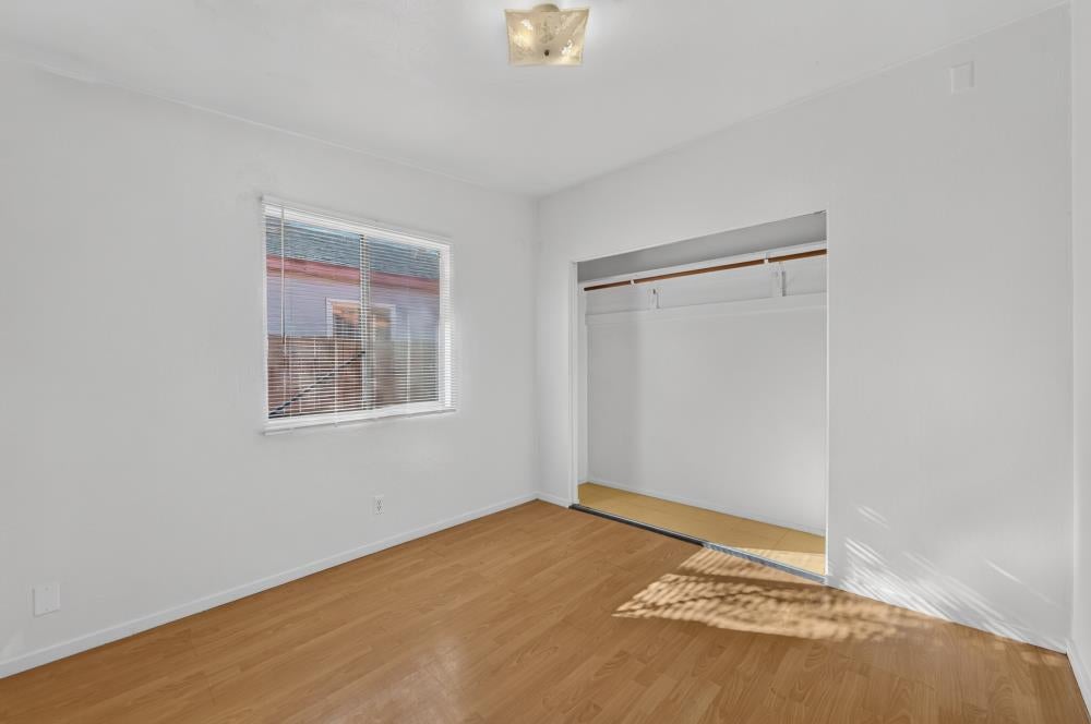 Empty bedroom with light wood flooring, window blinds, and an open closet.