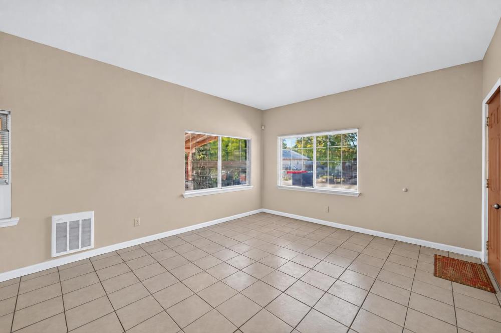 Vacant tiled room with beige walls, two windows, and a wooden door.