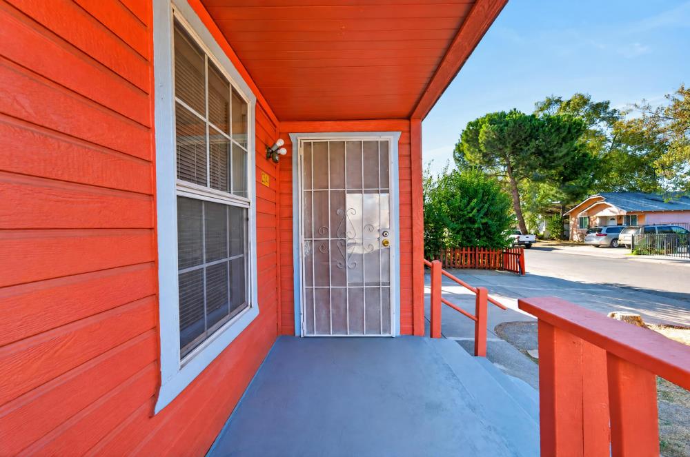 Red-sided home’s covered porch with a metal security door and red railing.