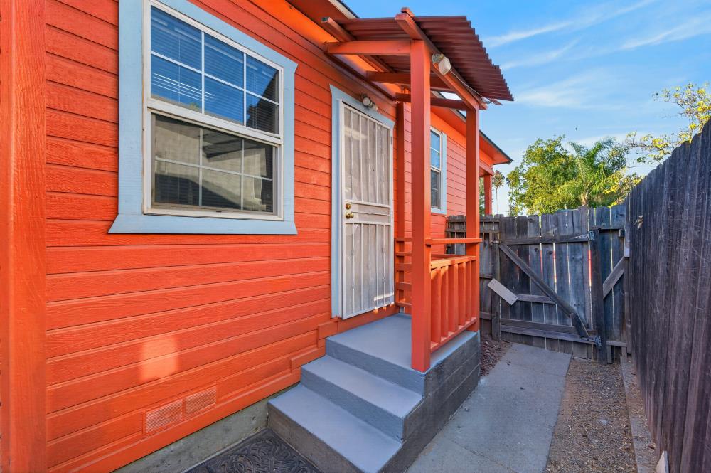Red-orange home exterior with a covered entry porch, gray steps, and a fenced side walkway.