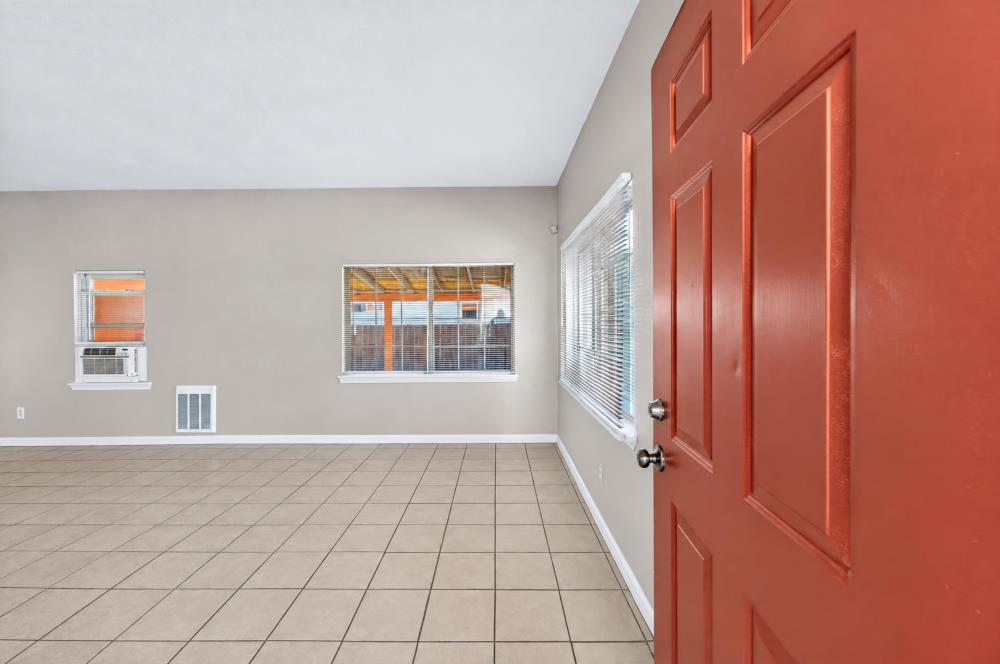 Vacant tiled room with a red entry door, several windows, and a window air conditioner.