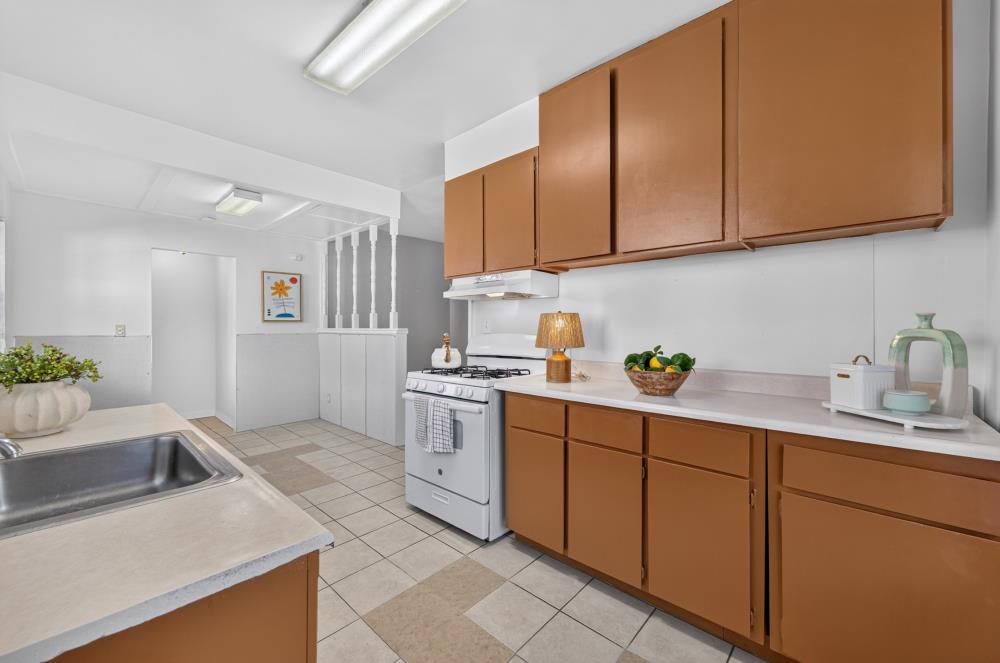 Kitchen with brown cabinets, a gas range, stainless-steel sink, and beige tile floor.