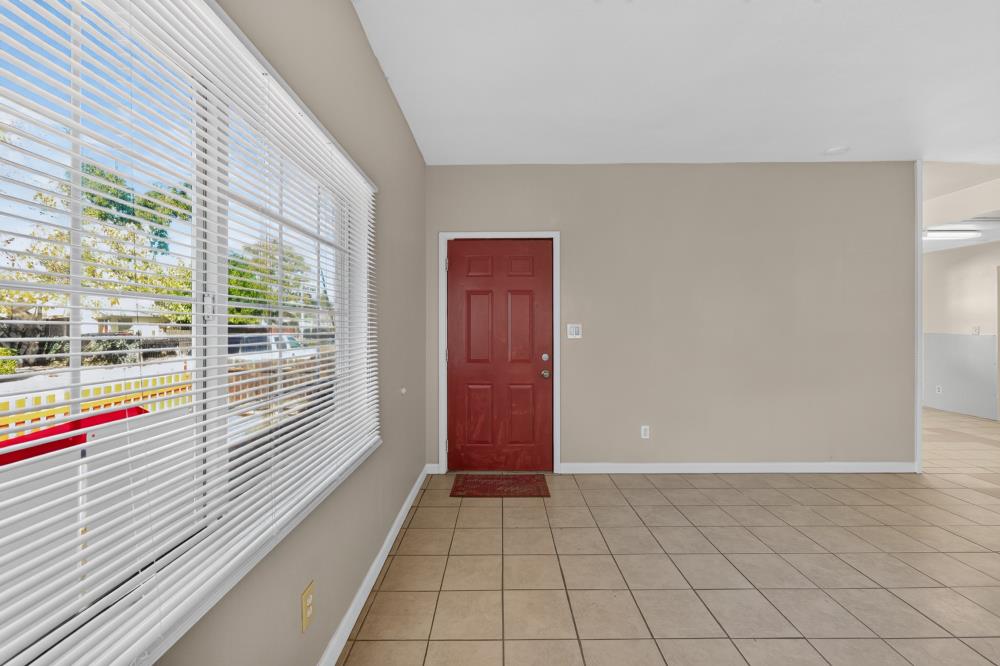 Empty tiled entryway with a red front door and large window with white blinds.