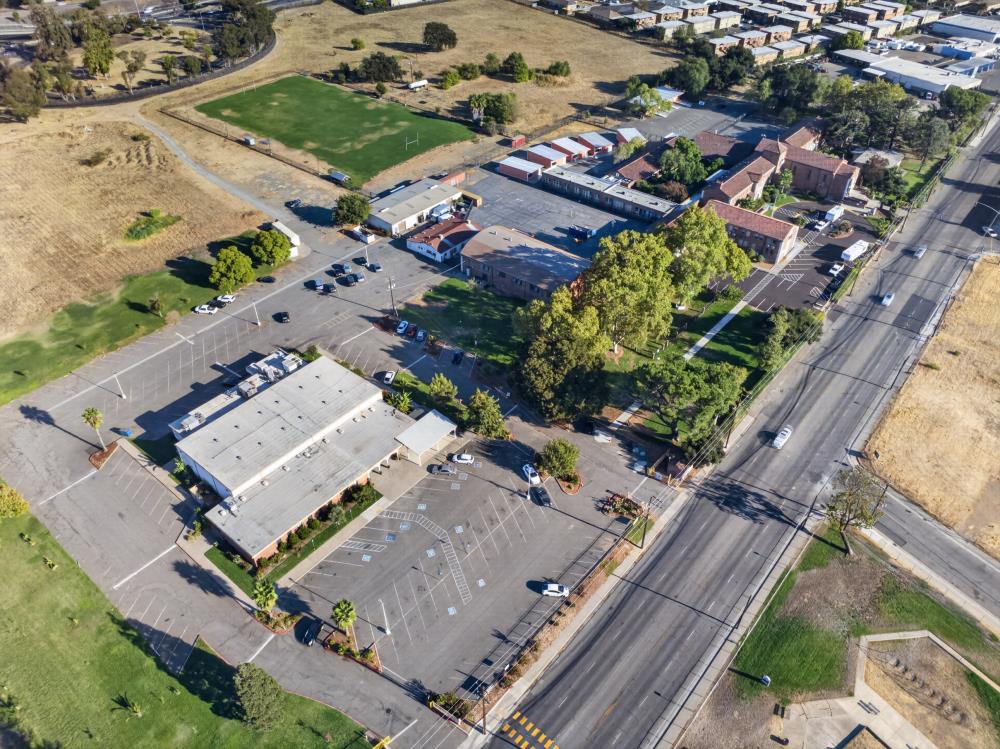 Aerial view of a building complex with large parking lots and a green sports field.