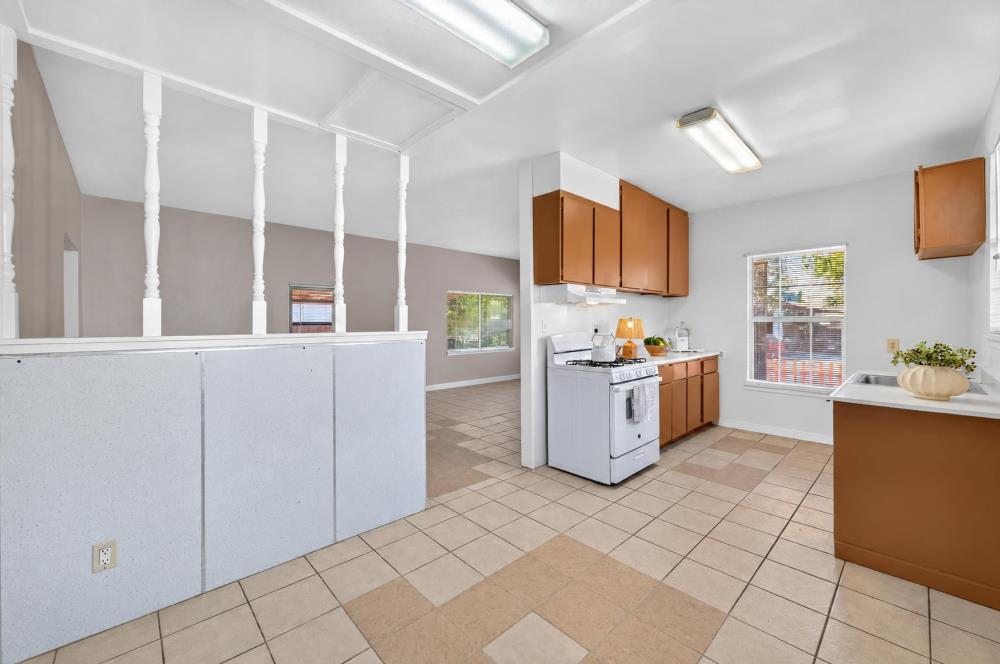 Kitchen with brown cabinets, white appliances, tiled floors, and a half-height partition.